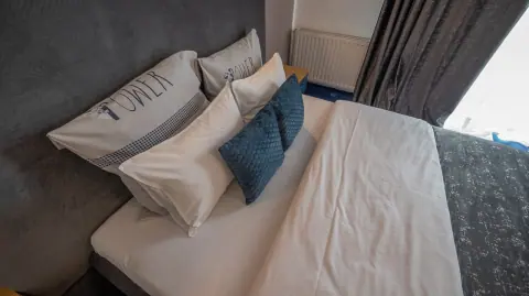 Bed linen and cushions against a grey headboard
